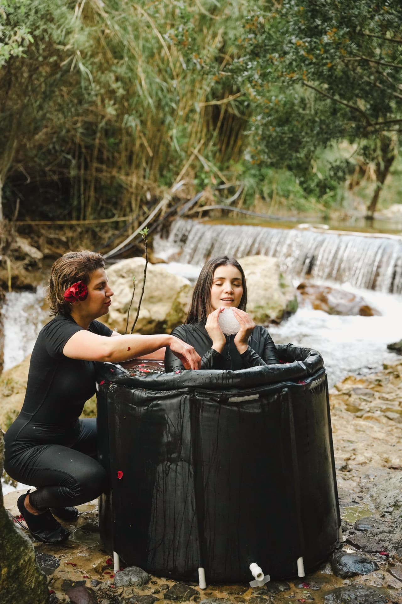 Zainab guiding a woman through a cold immersion beside a waterfall